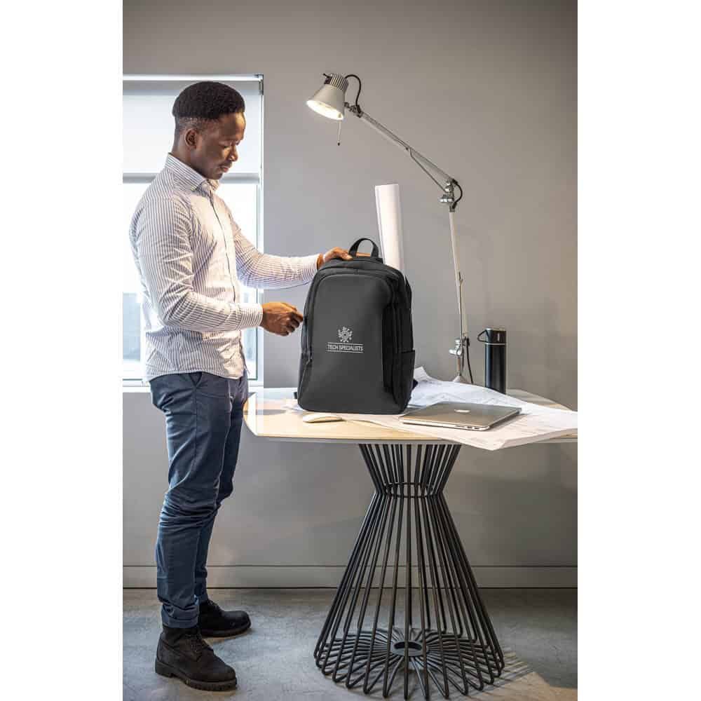Man packar en svart laptopryggsäck i ett kontorsmiljö, tillverkad av återvunnen polyester.